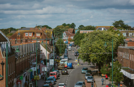 Looking north along Station Road New Milton with shops either side and cars on the road.